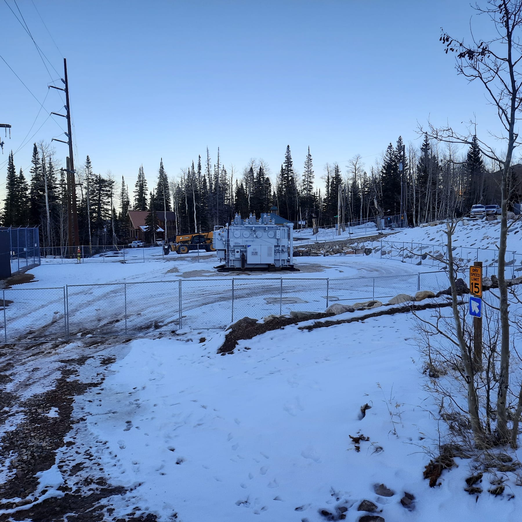 Temporary fence standing in snow around a power transfer station at Brian Head, aspens and pines behind it