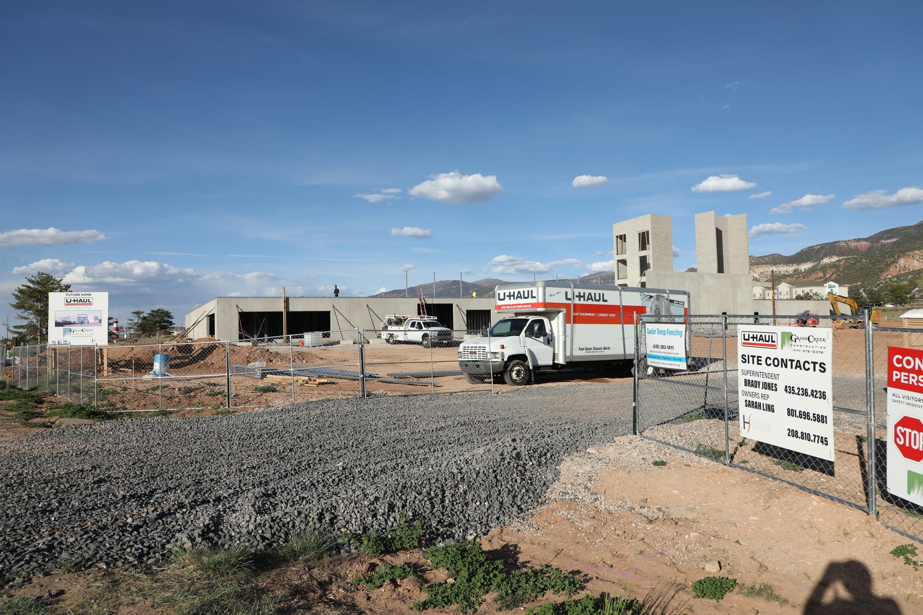 Temporary chain link fence around the U-Haul building under construction in Cedar City, U-Haul trucks and site contact signage behind the fence line