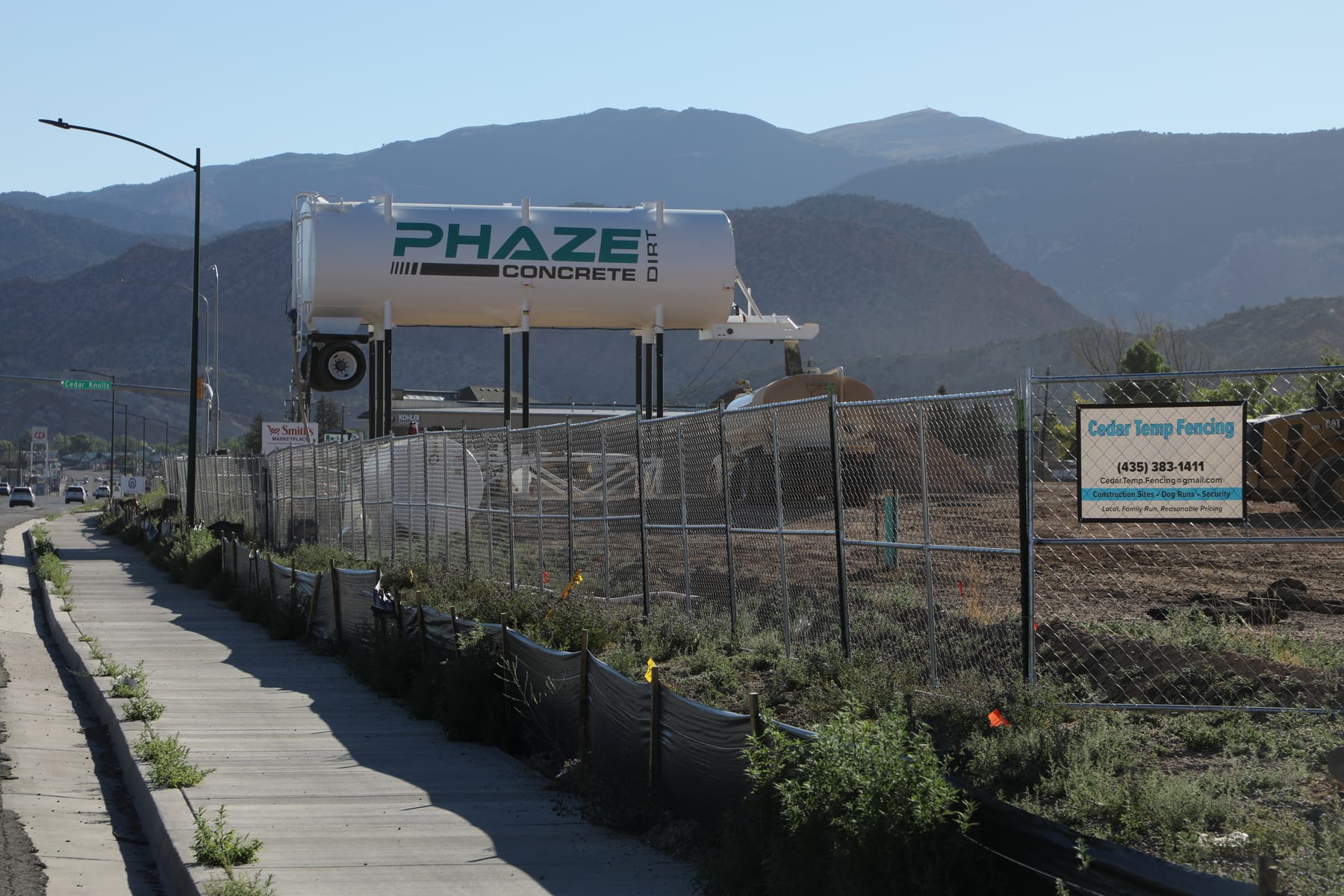 Temporary fence and silt fence running along the sidewalk at the new Smith's store site in Cedar City, mountains in the background